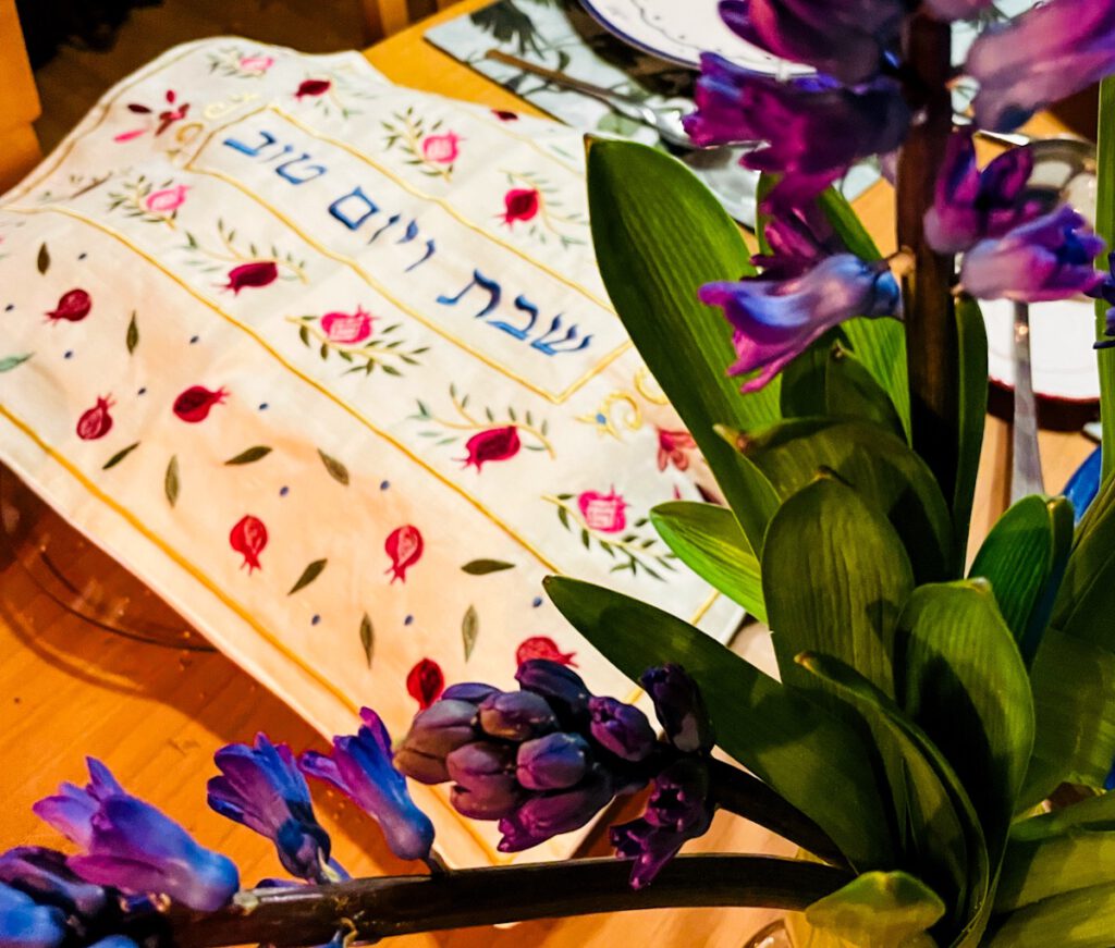 Eine Challa Decke auf einem Tisch mit lila Blumen.