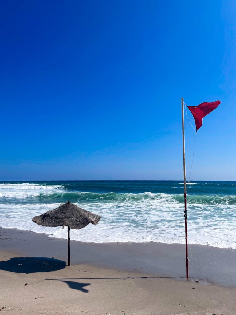 Eine rote Fahne die am Strand weht.