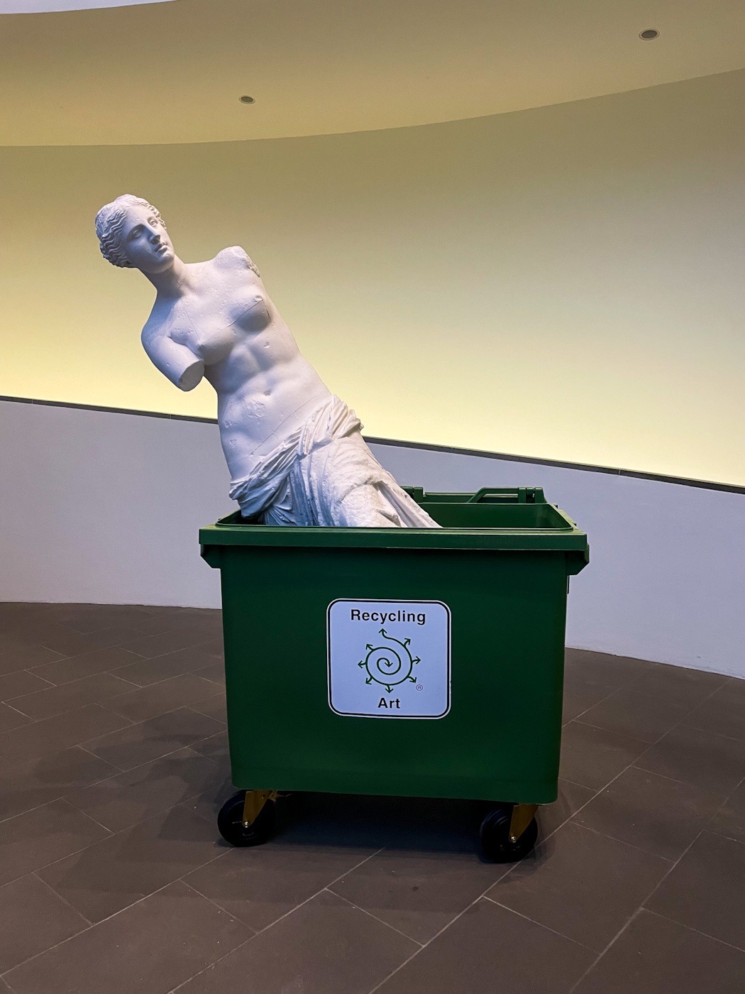Eine antik aussehende Skulptur einer Frau in einer grünen Mülltonne.