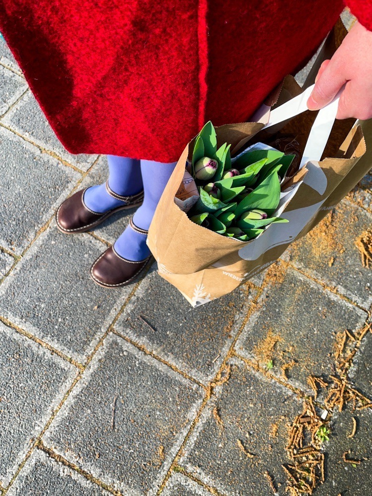 Frau mit Einkaufstasche. Darin lila Tulpen.