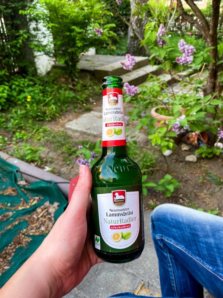 Ein Hand hält eine Bierflasche. Im Hintergrund ein Garten.